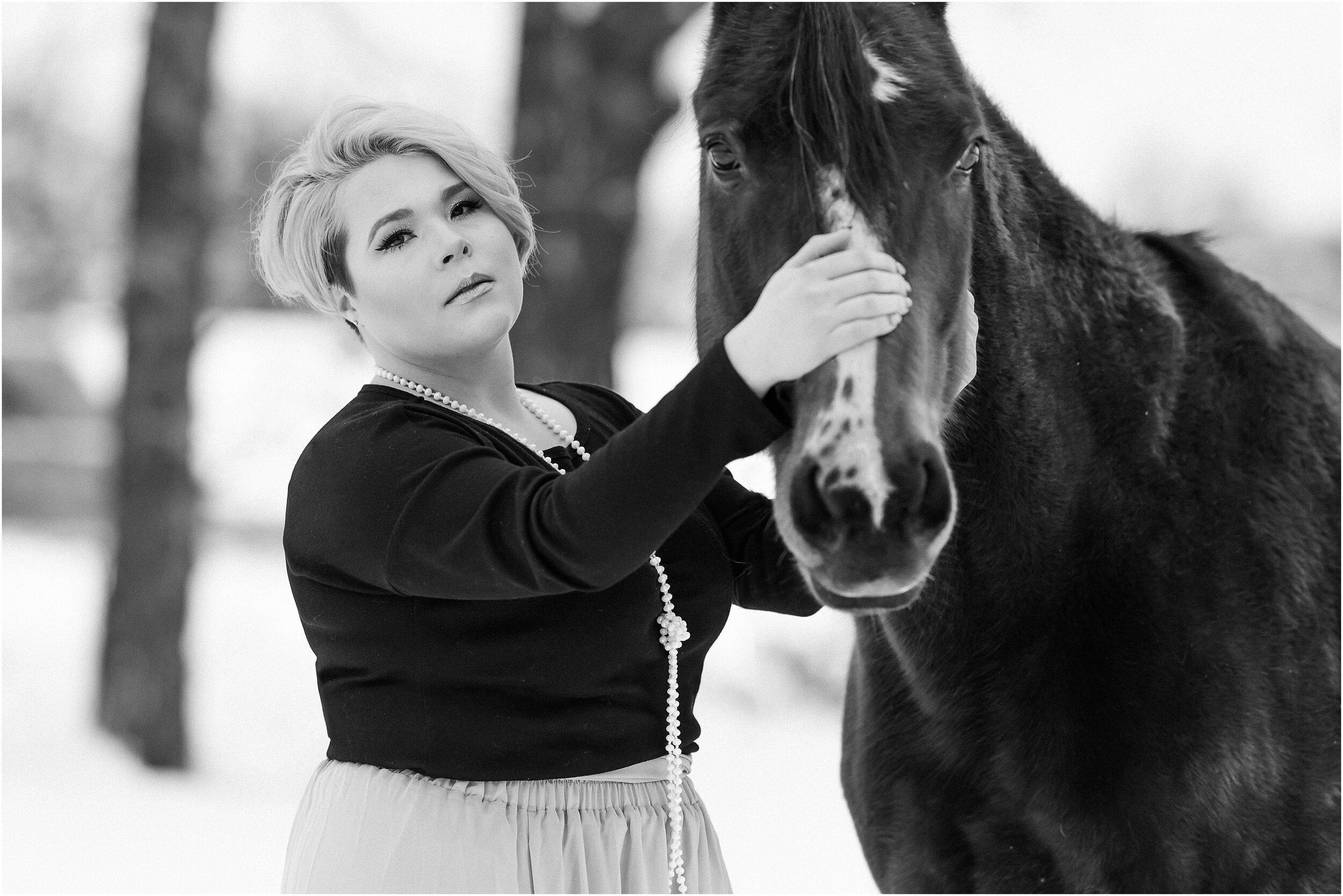  Black and white image of a Girl with grey hair in a pixie cut with her senior quarter horse mare, standing in the snow in Arcadia Oklahoma. Grey skirt outfit for equestrian portrait session 