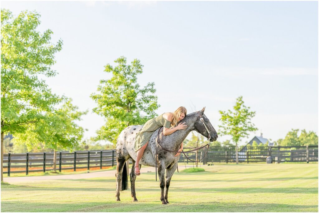 A blonde rider in a green dress sits on her Pony of the Americas mare while bareback. A manicured front lawn is a good location option for your equestrian portrait session