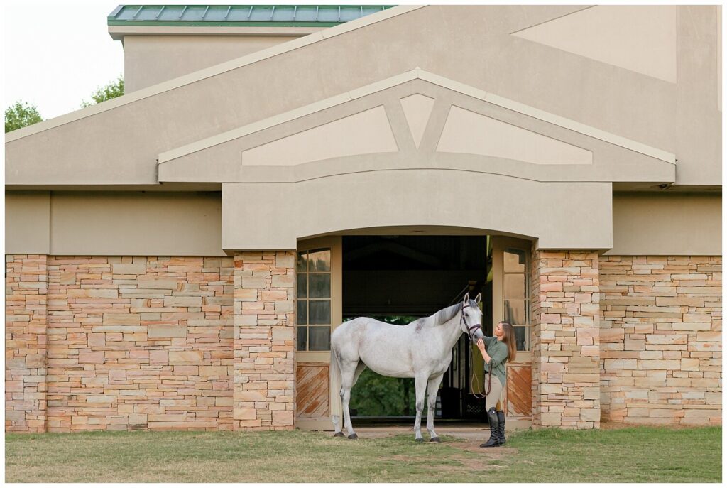 A woman pets her grey warmblood mare in front of Arcadia Hills Equestrian Center's stone barn. If your barn is particularly photogenic, use it as a portrait session location