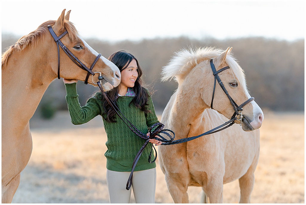 An equestrian girl in a green sweater snuggles with her two welsh ponies in Ardmore, OKlahoma