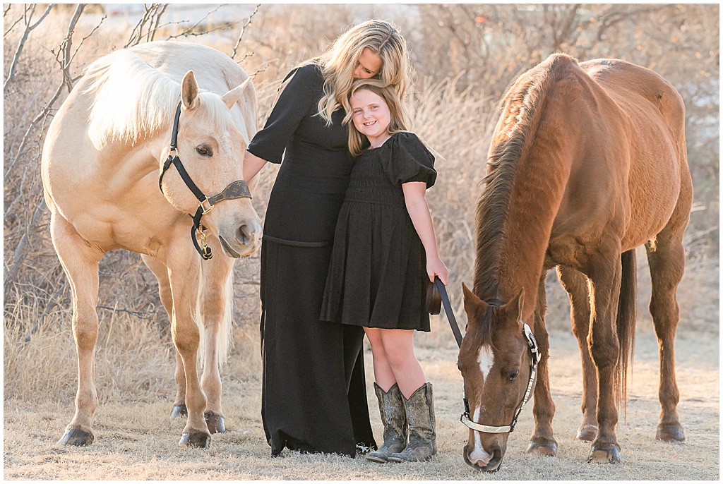 a mother and daughter embrace while their two horses graze on either side of them. Portraits taken in Big Spring texas