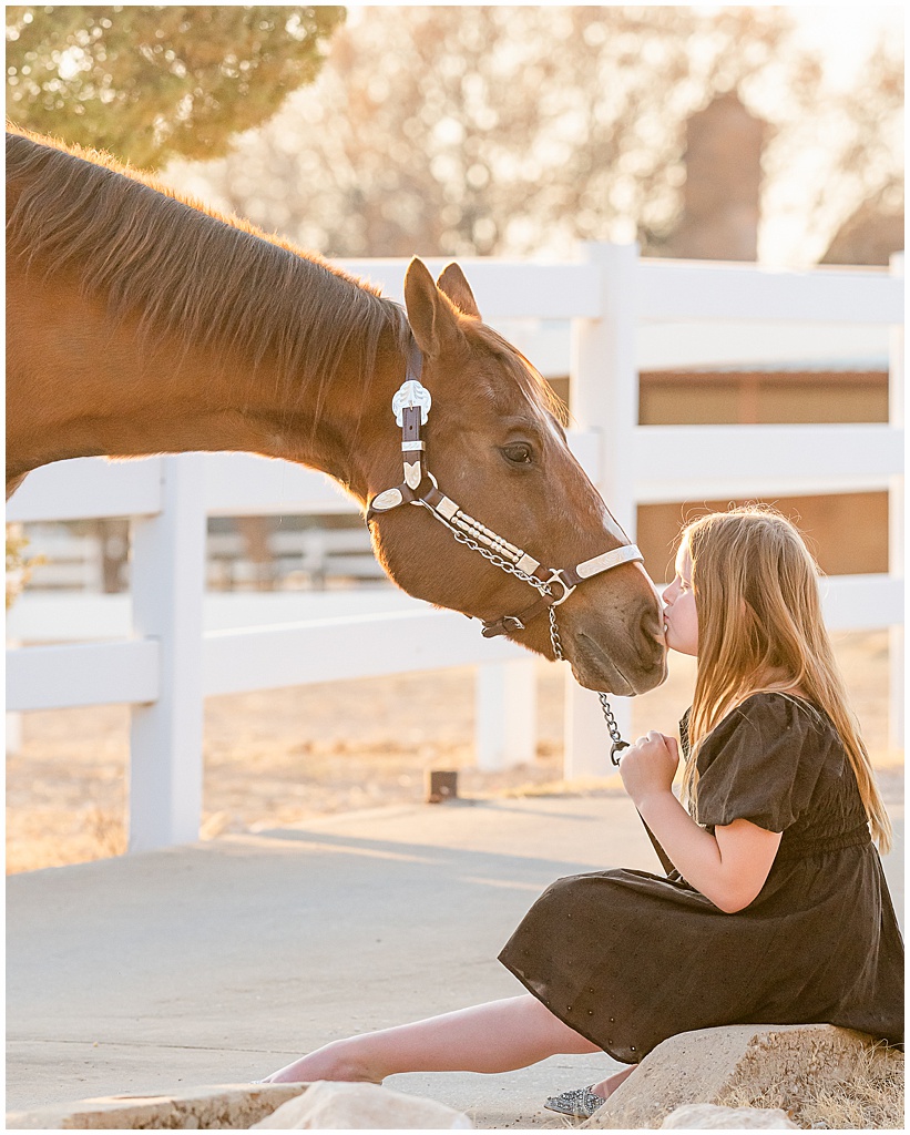 a young rider kisses the nose of her chestnut gelding while sitting on the ground in big spring, texas